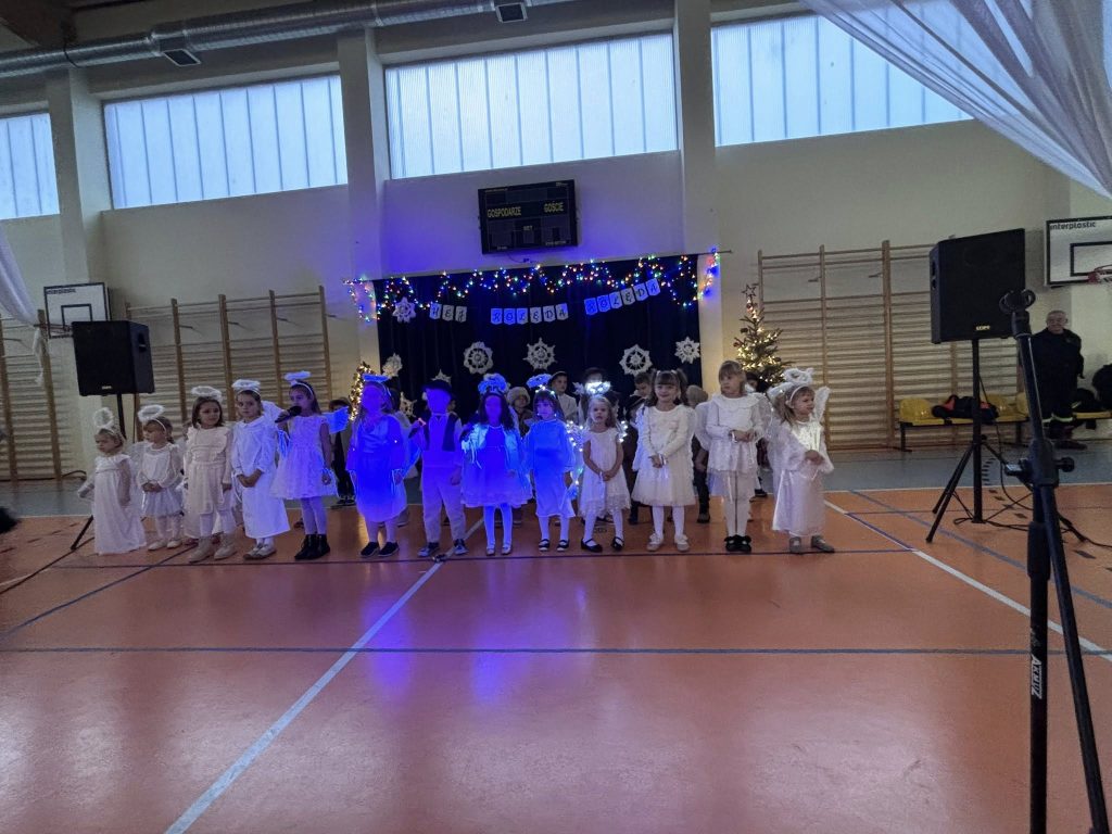 Stoisko edukacyjne przygotowane przez strażaków podczas Kiermaszu Świątecznego. Na stole znajdują się elementy wyposażenia strażackiego, a obok stoją strażacy w mundurach oraz odwiedzający.