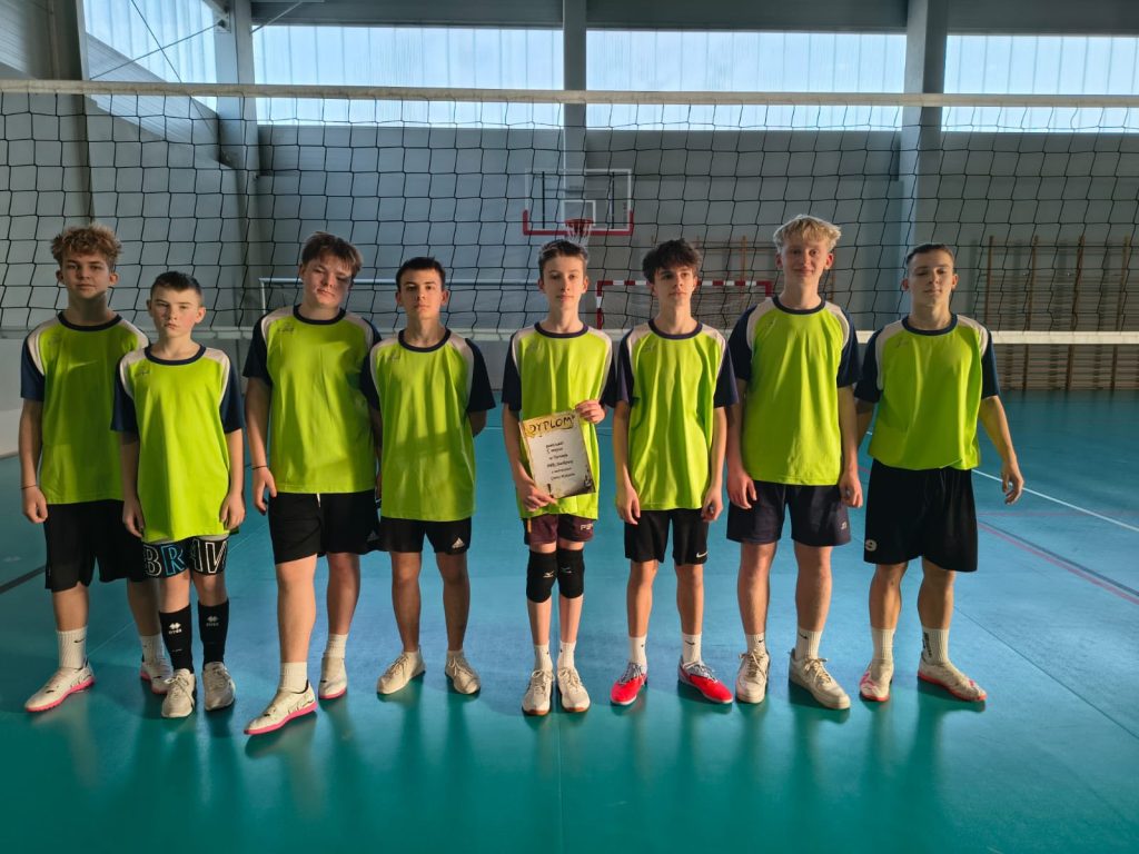 Grupowe zdjęcie drużyny siatkarskiej chłopców z ZSP w Borownie w zielonych strojach sportowych, stojących na hali sportowej, jeden z uczniów trzyma dyplom.