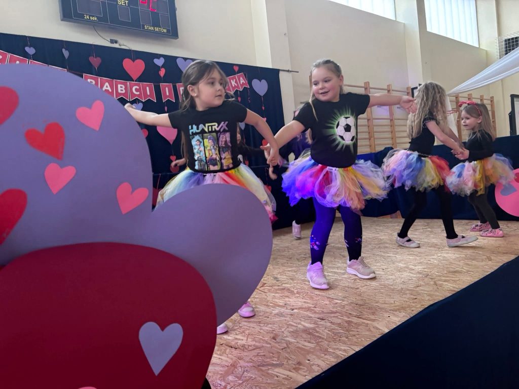 Dzieci tańczą na scenie w kolorowych strojach podczas występu artystycznego.