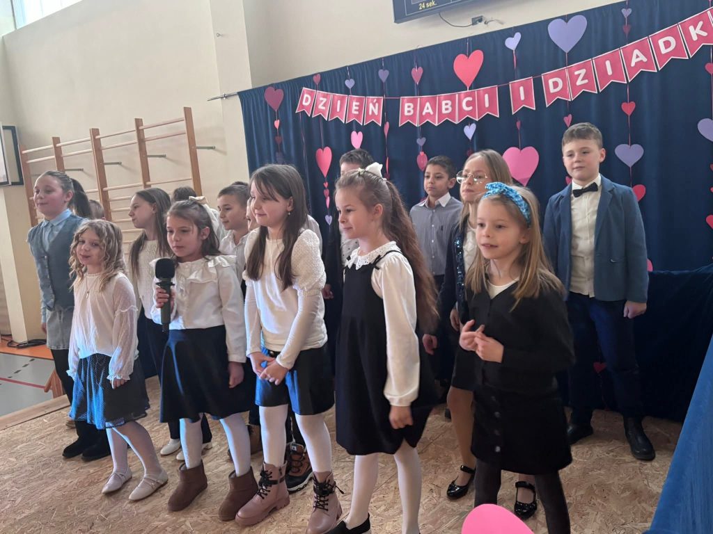 Grupa uczniów śpiewa na scenie podczas występu dla zaproszonych gości.