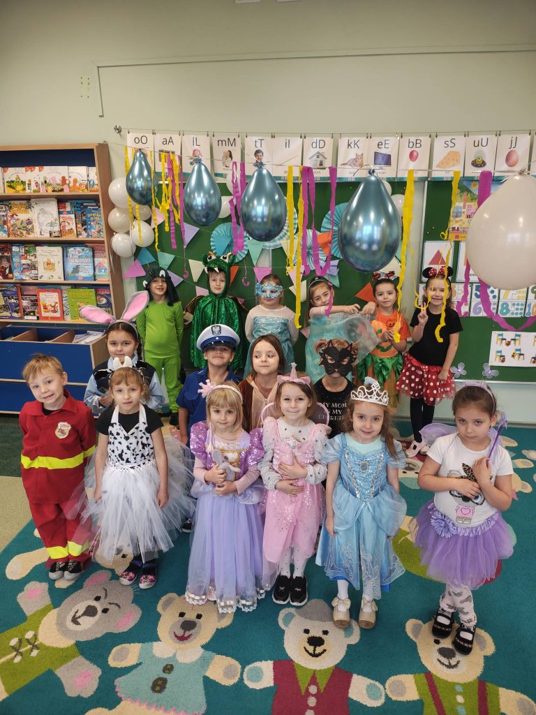 Dzieci w kolorowych przebraniach pozują do wspólnego zdjęcia podczas balu karnawałowego w przedszkolu.