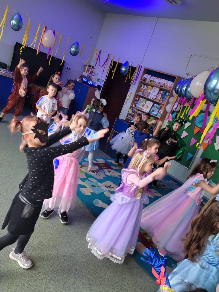 Dzieci tańczą i bawią się w sali przedszkolnej podczas balu karnawałowego.