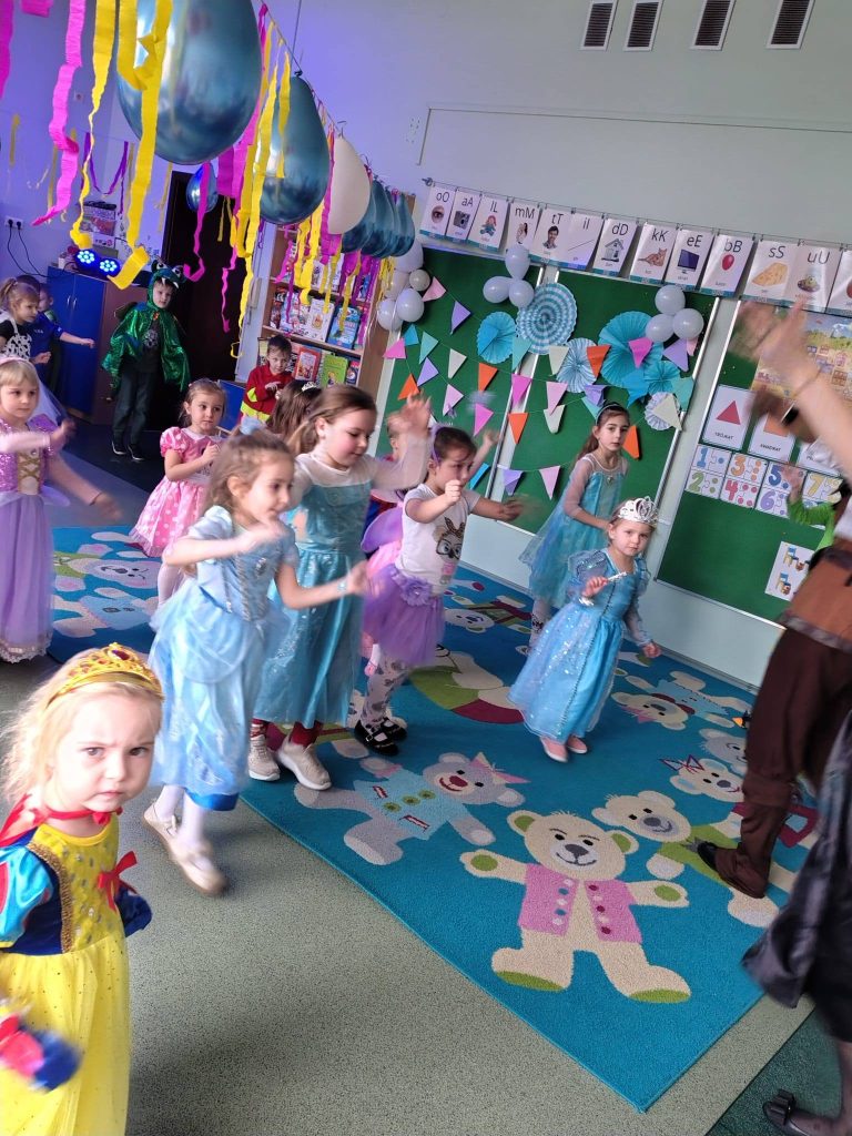 Przedszkolaki w strojach karnawałowych uczestniczą w zabawach ruchowych podczas balu.