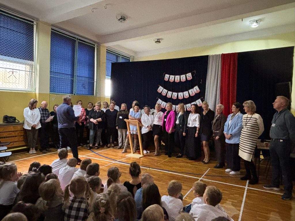 Dzień Edukacji Narodowej: społeczność szkolna stoi na scenie w sali gimnastycznej, z przodu siedzą uczniowie.