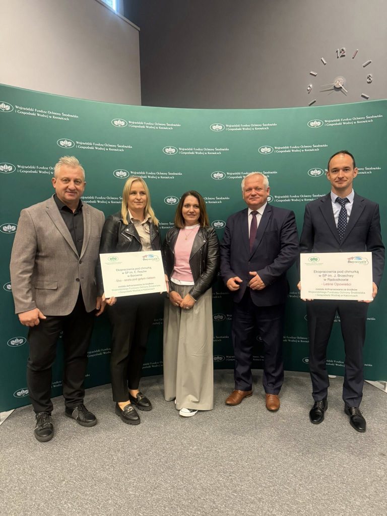 Grupa pięciu dorosłych osób stojących przed zieloną ścianką Wojewódzkiego Funduszu Ochrony Środowiska i Gospodarki Wodnej w Katowicach. Dwie osoby trzymają certyfikaty dotyczące realizacji projektów ekologicznych.