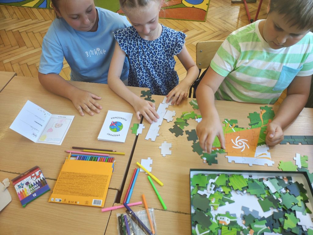 Dzieci wspólnie układają puzzle przy stoliku podczas zajęć szkolnych.