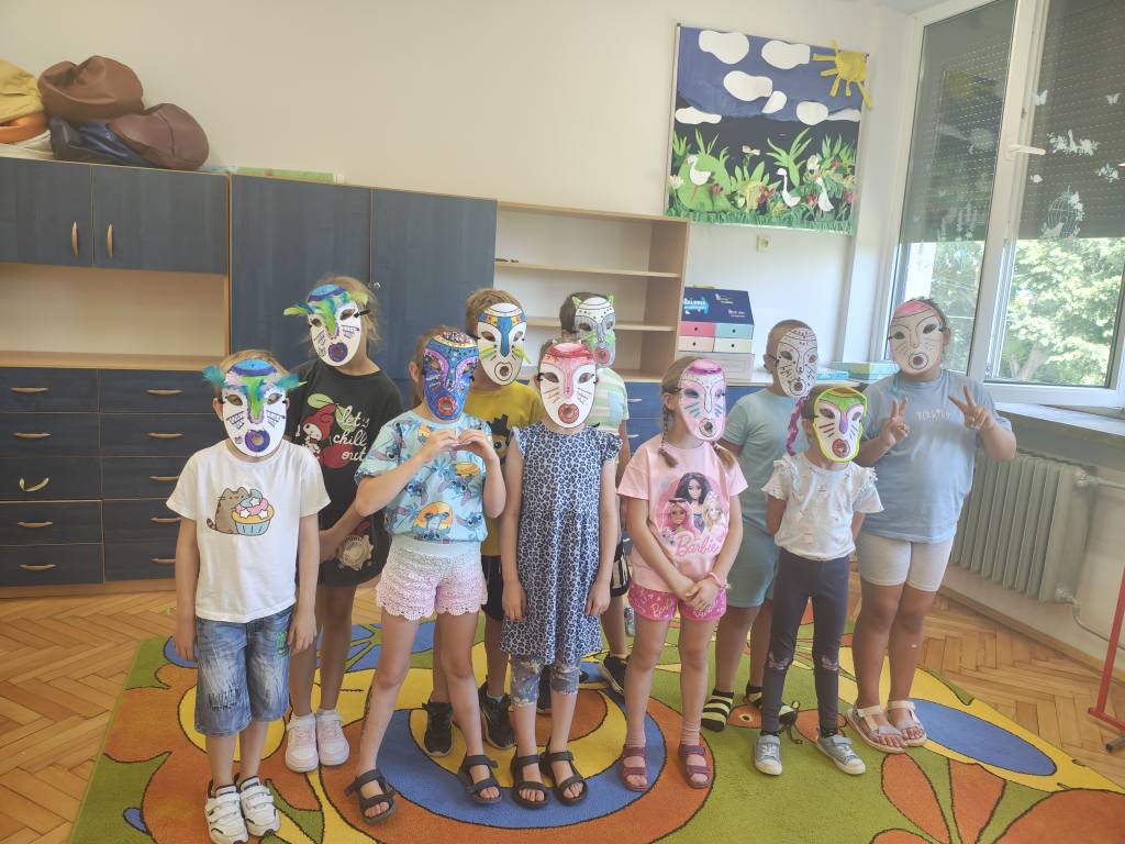 Dzieci prezentują własnoręcznie wykonane kolorowe maski w sali lekcyjnej.