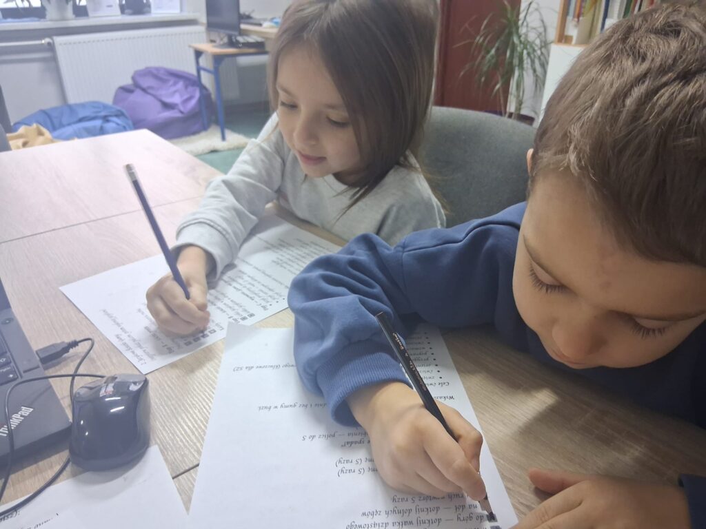 Dziewczynka i chłopiec siedzą przy stole i piszą ołówkiem na kartkach z zadaniem.